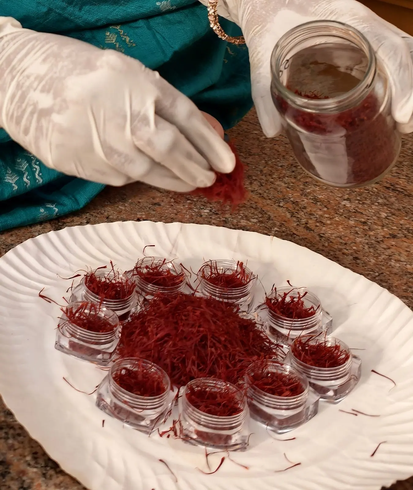 Gloved hands filling small jars with dried saffron threads
